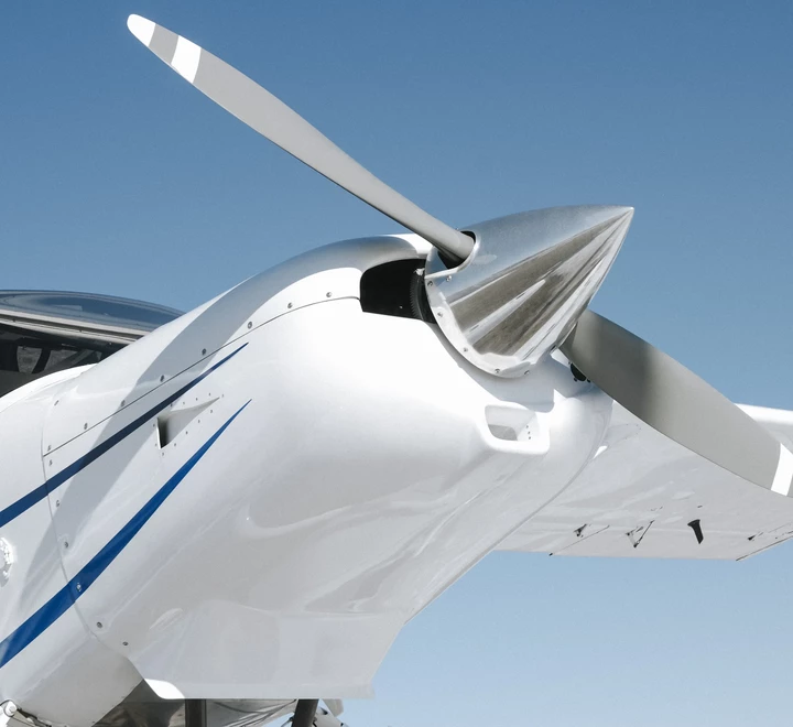 A photo of a Cessna, small private airplane. Composition taken with one side propeller close to viewer. Blue sky in the background. 