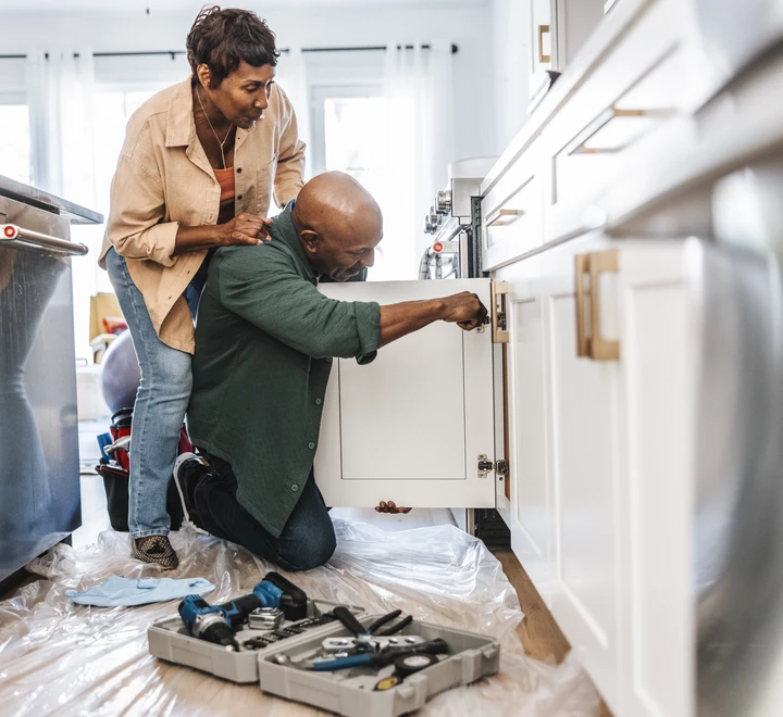 Senior couple repairing or installing white, kitchen cabinet doors in a residential home. 