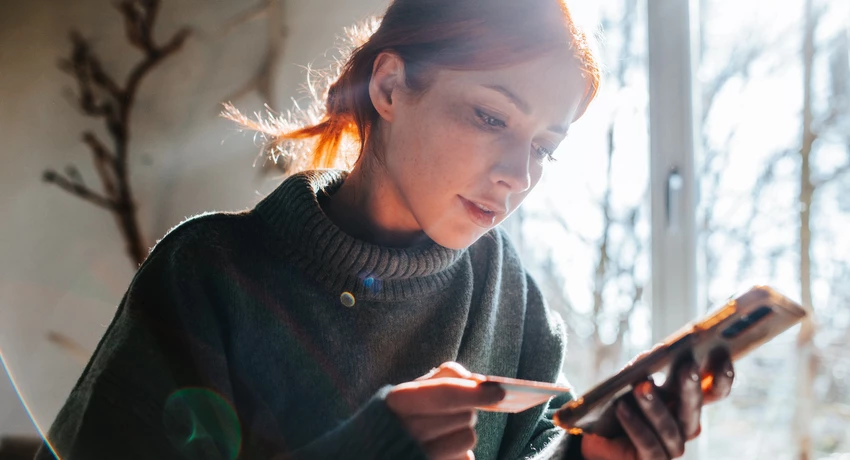 Young woman shopping online with phone and credit card. Woman is looking at the phone; credit card is in her hand. 