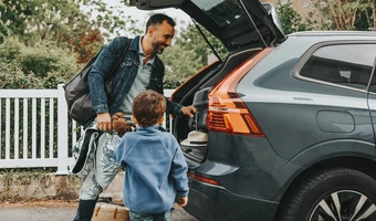 Smiling man loading luggage with son standing near car trunk. 