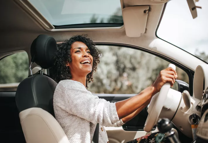 Smiling young African American woman driving car. 